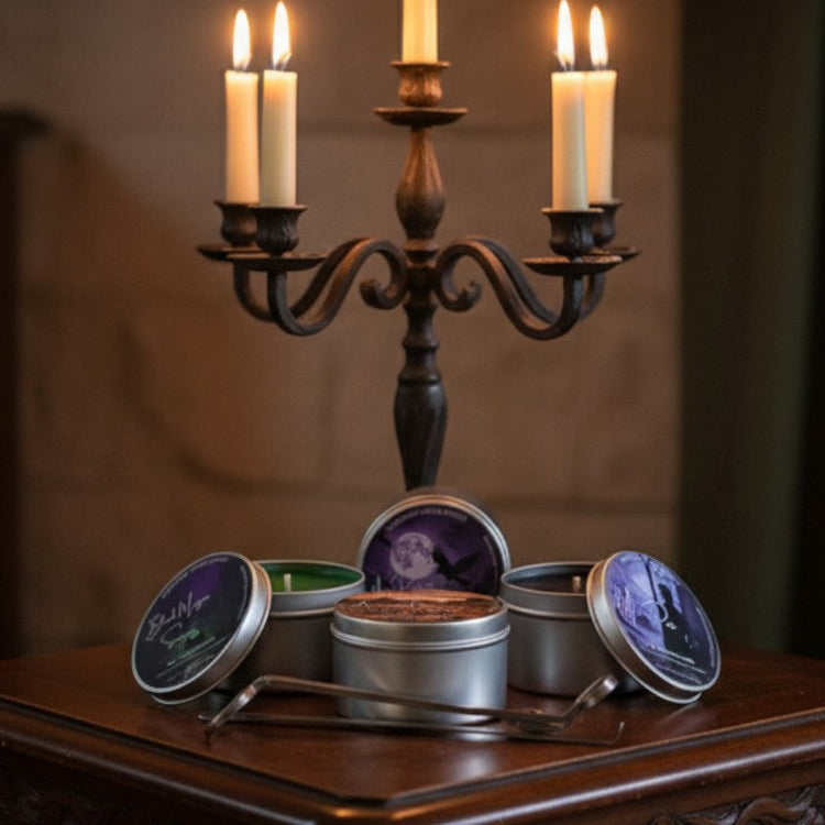 Four candle tins with Whispering Woods Soapery labels on a wood table with a lit candelabra