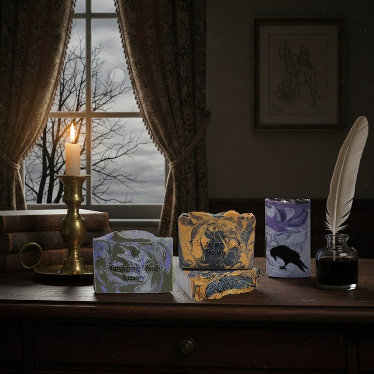 A collection of three different soaps sit on a writing desk in a study. There is quill and ink, books and a candlestick on the desk.