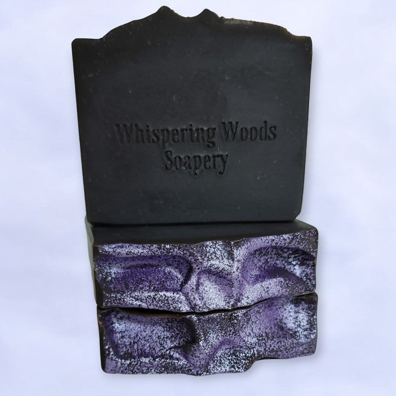 Three bars of black soap with purple tops against a very light purple background