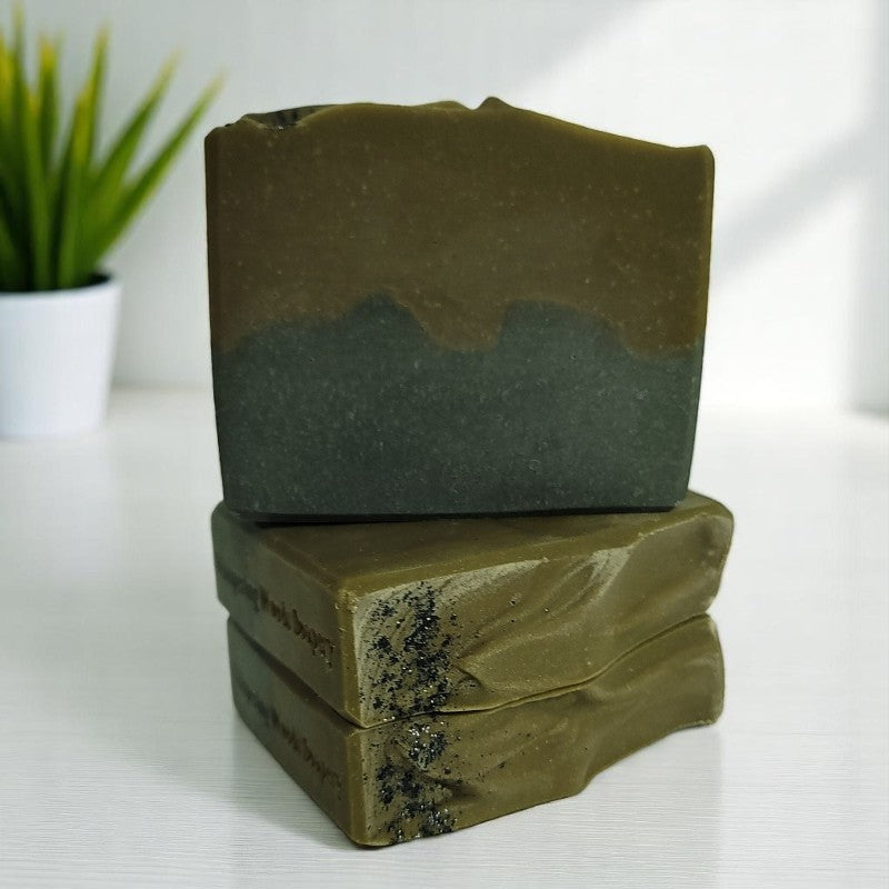 Three greenish-brown and black bars of soap on a white surface