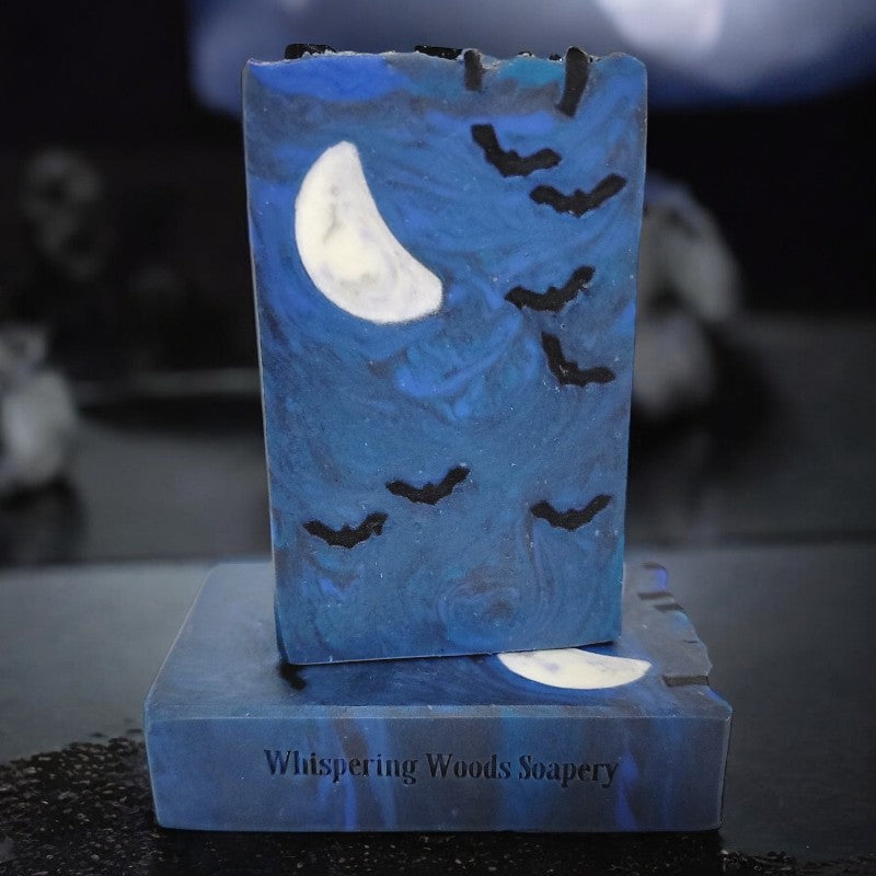 Two blue bars of soap with seven small bats and a crescent moon embed on a black counter with a black and white eerie background