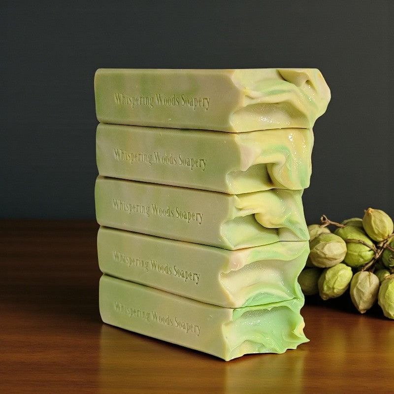 Stack of soap bars with 'Whispering Woods Soapery' branding on a wooden surface