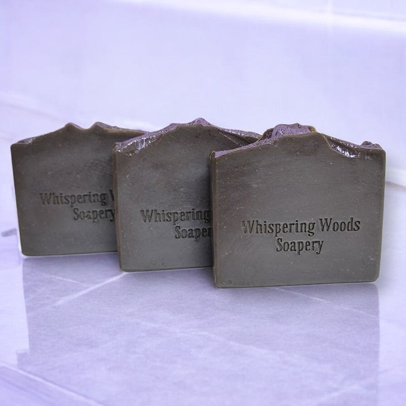 Three bars of black soap with light purple tops sit side by side on a marble surface
