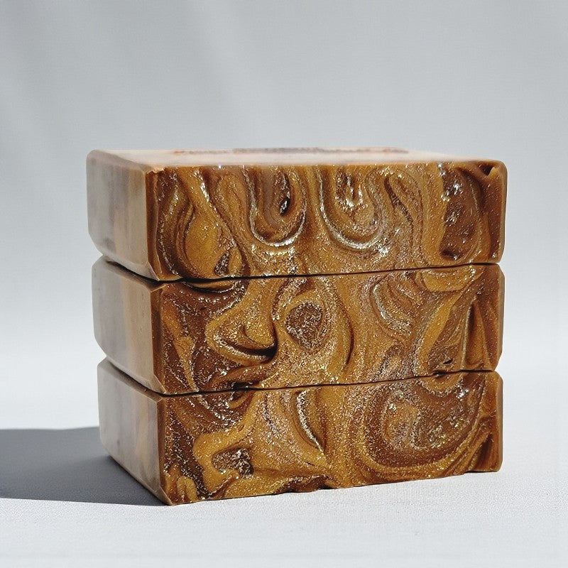 Three stacked soap bars in hues of butterscotch gold and brown on a light gray background