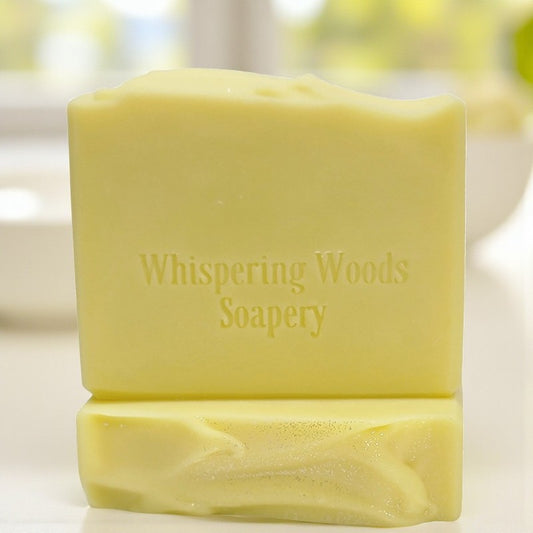 Bars of yellow soap with 'Whispering Woods Soapery' branding on a blurred natural background