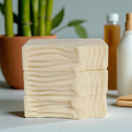 Cream bars of soap on a light background with a plant and bottles in the background