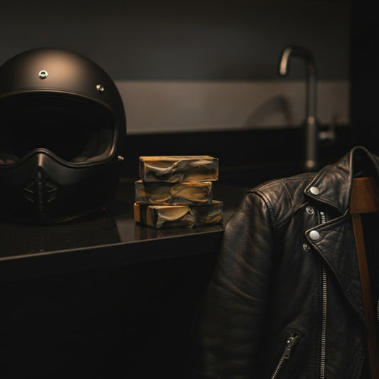 Black helmet and stack of soap bars on a black counter, with a black leather jacket hanging off a chair