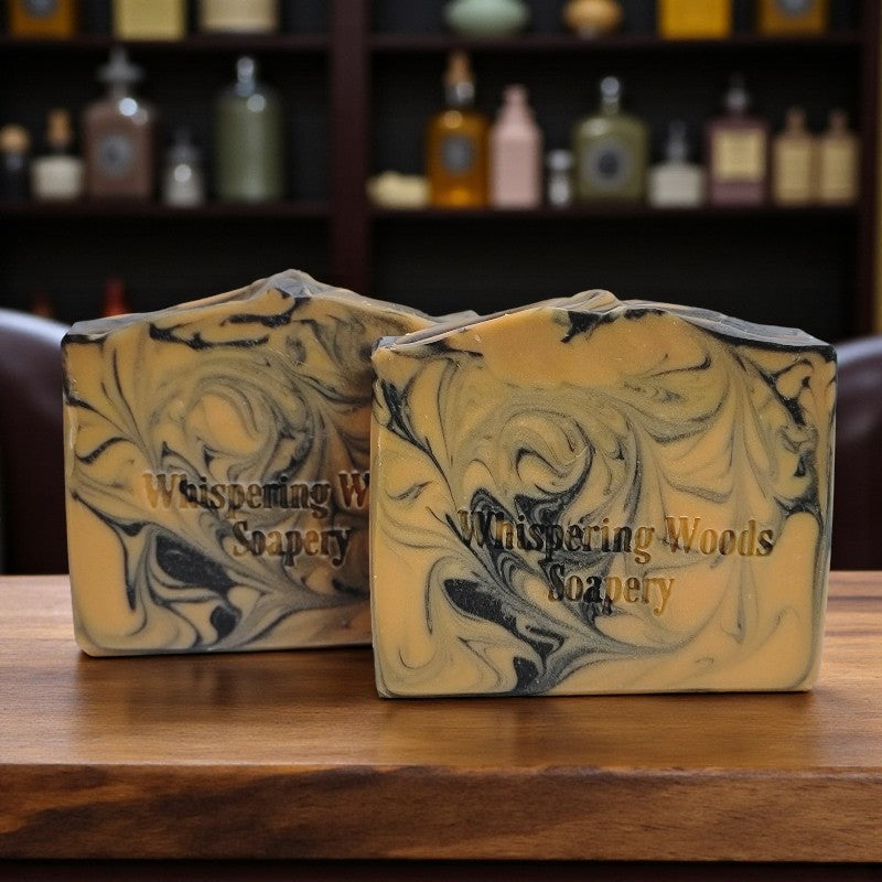 Two soap bars with a marbled design on a wooden surface, branded 'Whispering Woods Soapery'