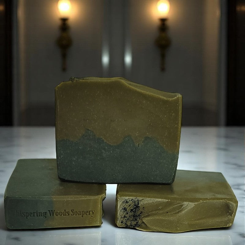 Three greenish-brown and black bars of soap on a granite countertop in a dim-lit room with sconce lighting