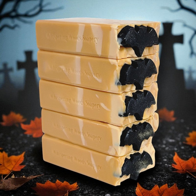 Stack of Halloween-themed soap bars with black bats on top, with a dark background with cross gravestones and leaves
