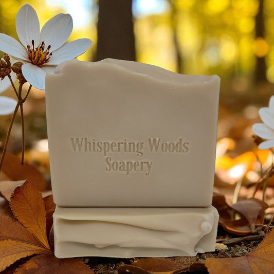 Two tan bars of soap branded 'Whispering Woods Soapery' with white flowers and autumn leaves