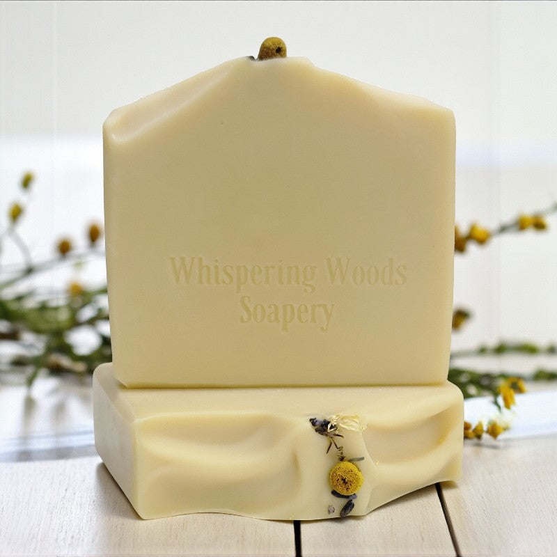 Bars of soap with 'Whispering Woods Soapery' branding on a wooden surface with blurred natural background