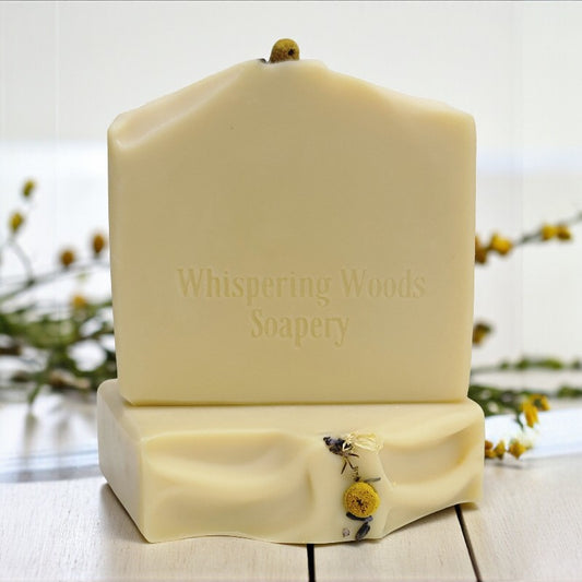 Bars of soap with 'Whispering Woods Soapery' branding on a wooden surface with blurred natural background