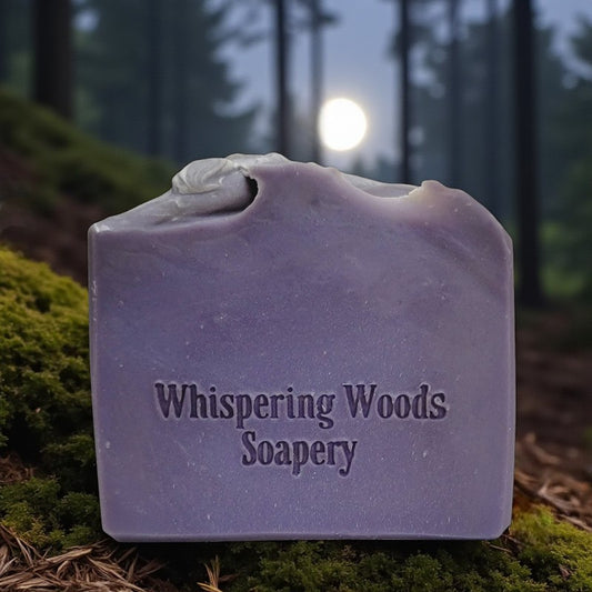 Purple soap bar with 'Whispering Woods Soapery' text on a forest background