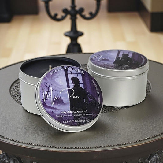 Two silver candle tins with purple labels featuring a silhouette of a person on a dark background are placed on a round wood table