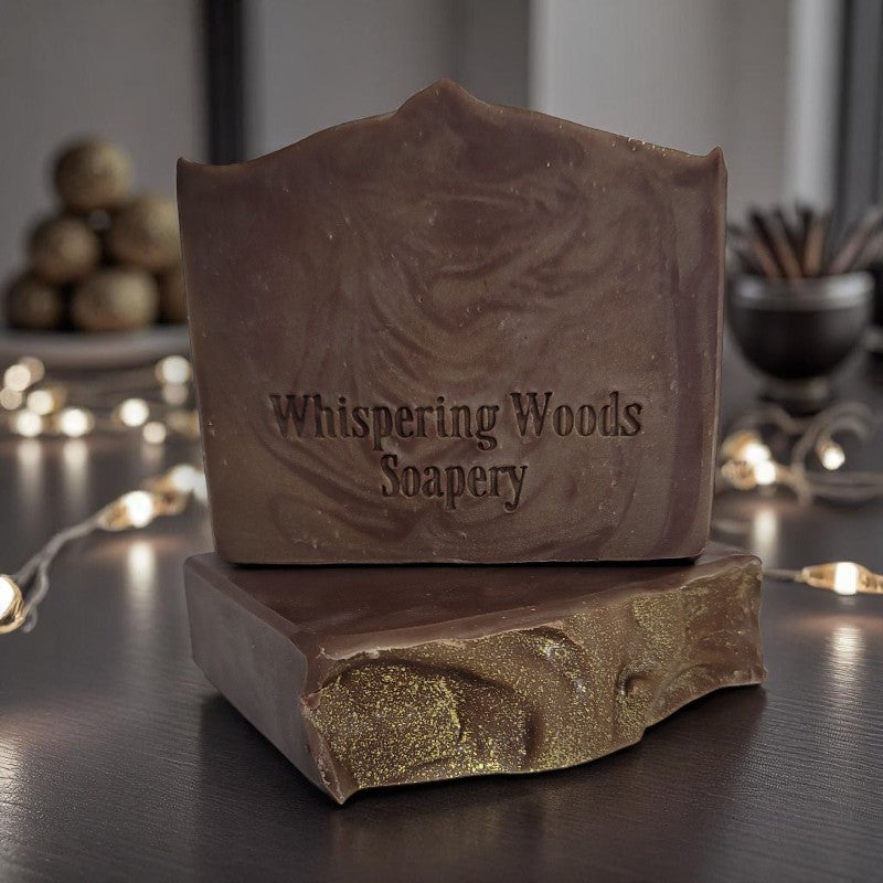 Two bars of brown-swirled soap with sparkly gold tops sit on a table with fairy lights and decorations in the background