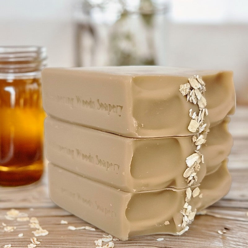 Three pale-brown bars of soap on a wood table with a jar of honey