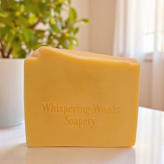Bar of soap with 'Whispering Woods Soapery' branding on a light surface