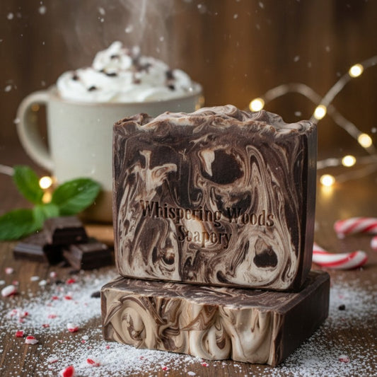 Two bars of 'Whispering Woods Soapery' soap stacked with a mug of hot chocolate and candy canes in the background