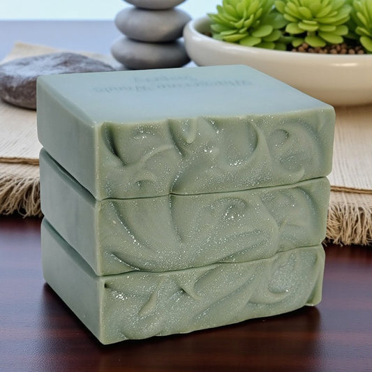 Three stacked blue-green soap bars with textured tops sit on a wooden surface