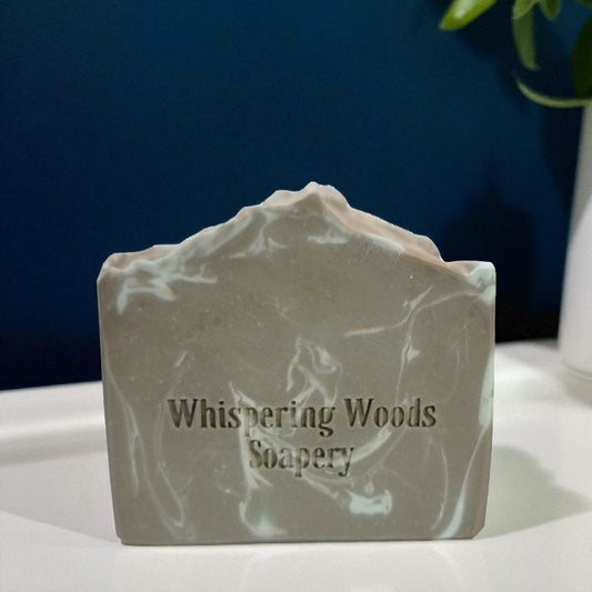 A marble green soap with branding 'Whispering Woods Soapery' sits on a white surface
