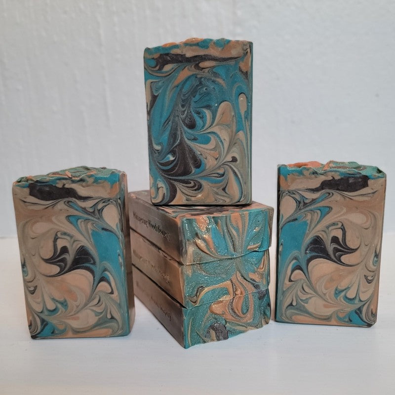 Six rectangular soap bars with teal, brown, orange and champagne swirls stand on a white surface.