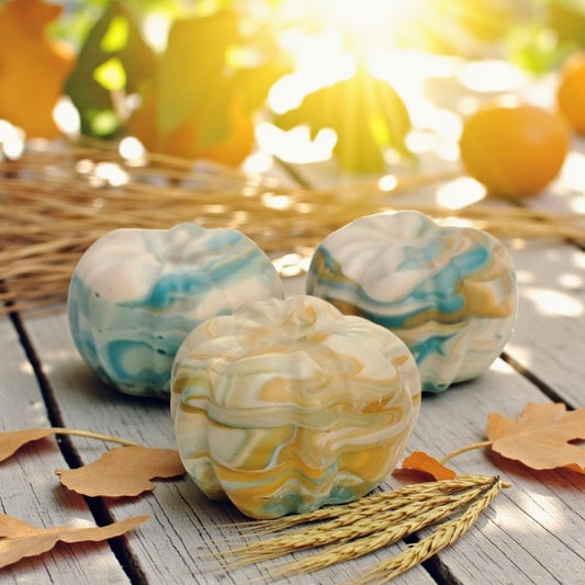 Teal, cream and orange swirled pumpkin soaps on a wooden surface with autumn leaves and sunlight in background