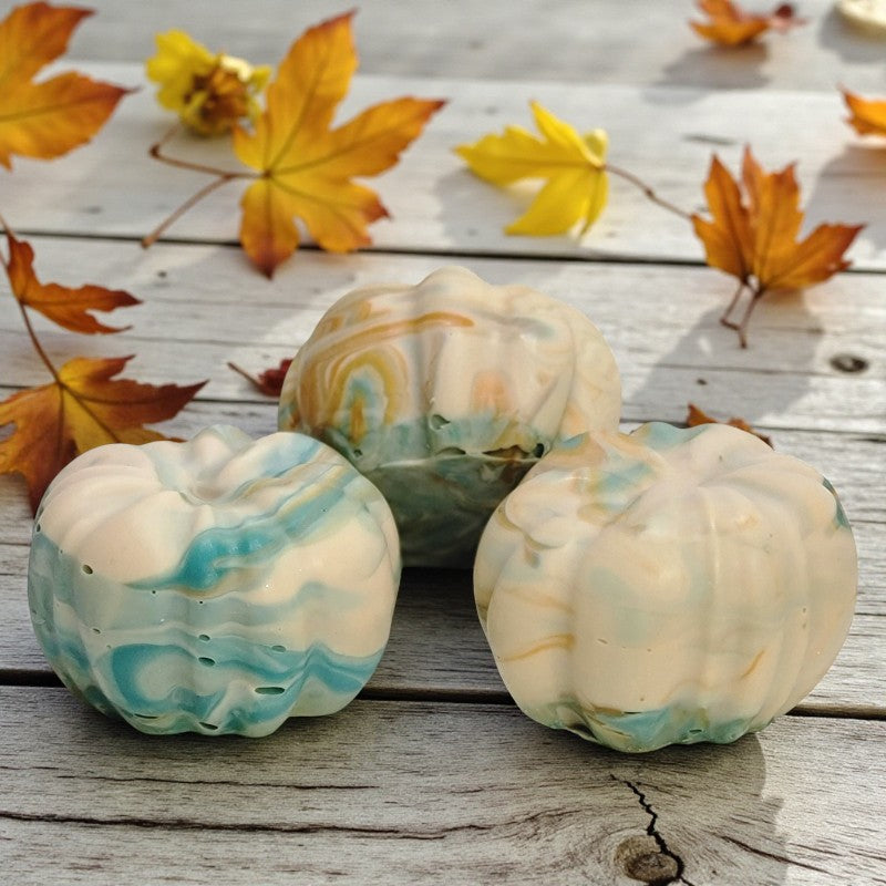 Soap pumpkins with cream, teal and orange swirls on a wooden surface with autumn leaves