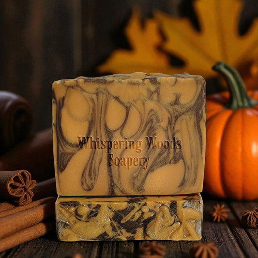 Two orange and brown soap bars on a wood table with a pumpkin and spices
