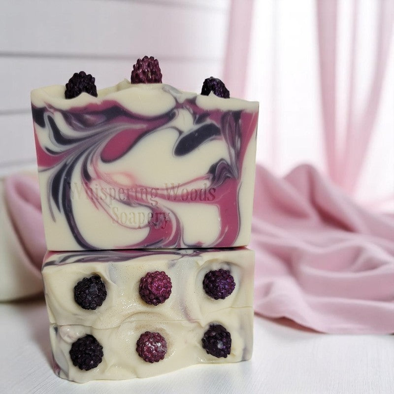Three white soaps with purple and pink swirls on a white surface with pink sheer fabric in the background