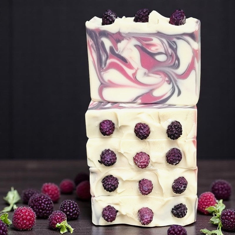 Five white soaps with purple and pink swirls on a dark table with raspberries