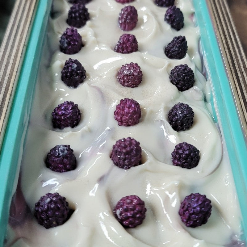 Close-up view of freshly poured creamy white soap with pink and purple berries placed on top