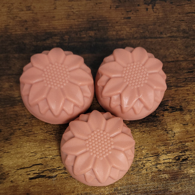 Three rose-clay-colored flower facial soaps on a wooden surface