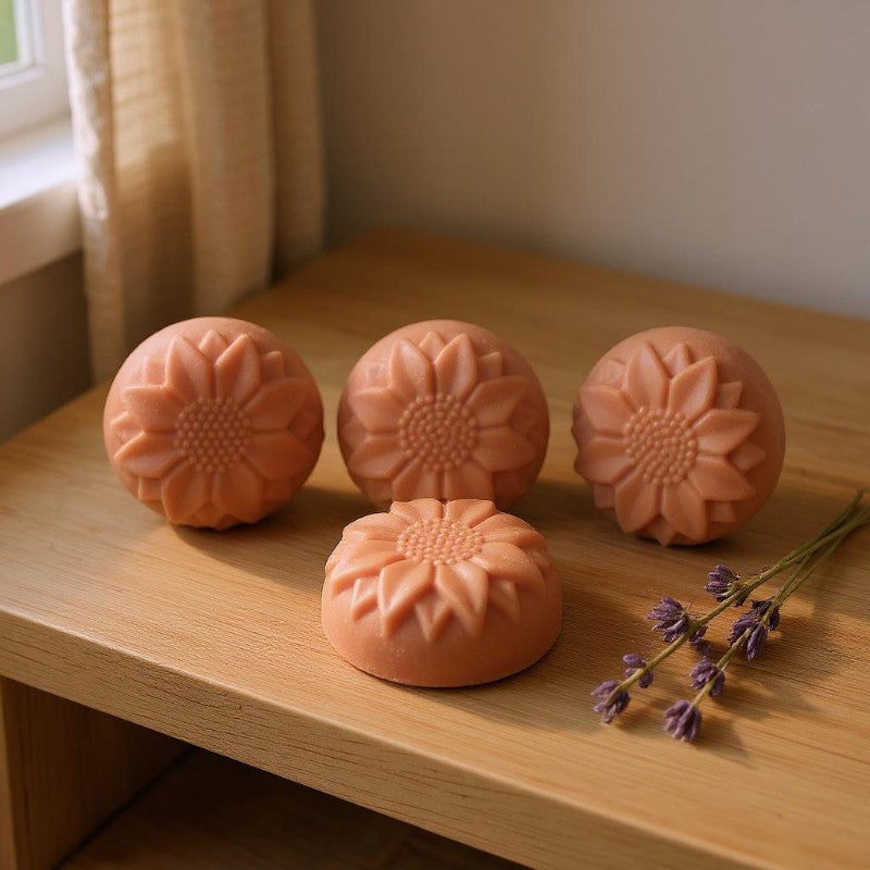 Four rose clay sunflower-shaped facial soaps on a wooden surface with a window in the background