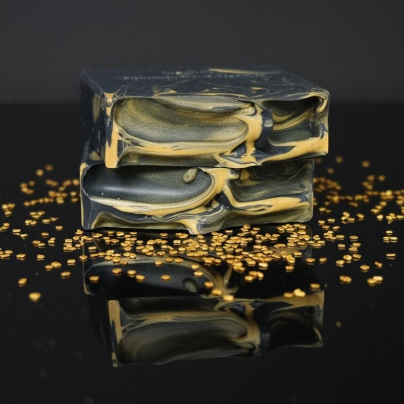 Marbled black and gold soap bars with gold glitter sprinkled on a reflective surface
