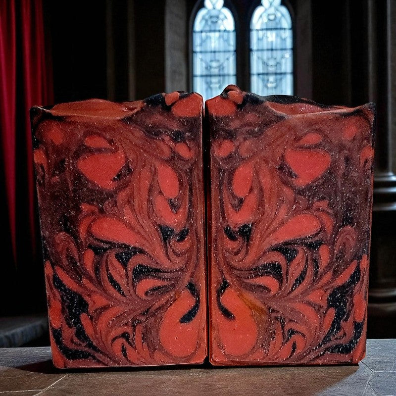 Decorative soap bars with intricate red and black design on a dark surface with gothic windows behind them