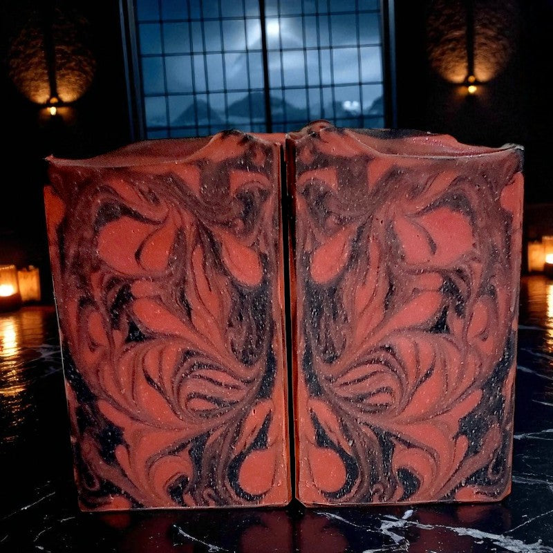 Two red and black swirled soaps on a black marbled surface with candles lit in the background