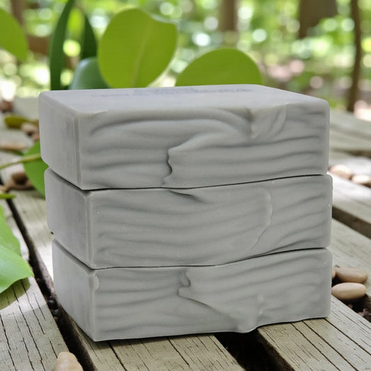 Stack of three silver bars of soap on a wooden surface with greenery in the background