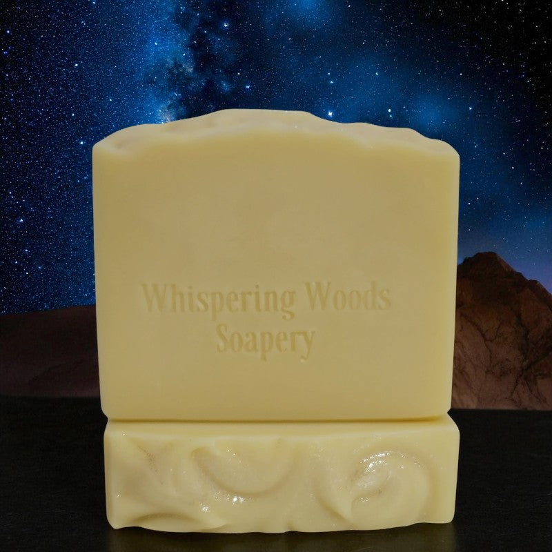 Bars of pale yellow soap with 'Whispering Woods Soapery' branding against a starry night sky background