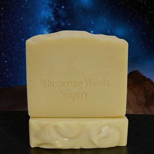 Bars of pale yellow soap with 'Whispering Woods Soapery' branding against a starry night sky background