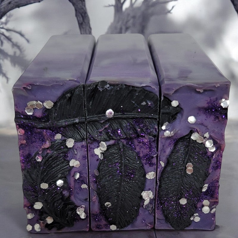 Close-up view of purple and silver soap tops with silver glitter and raven feathers