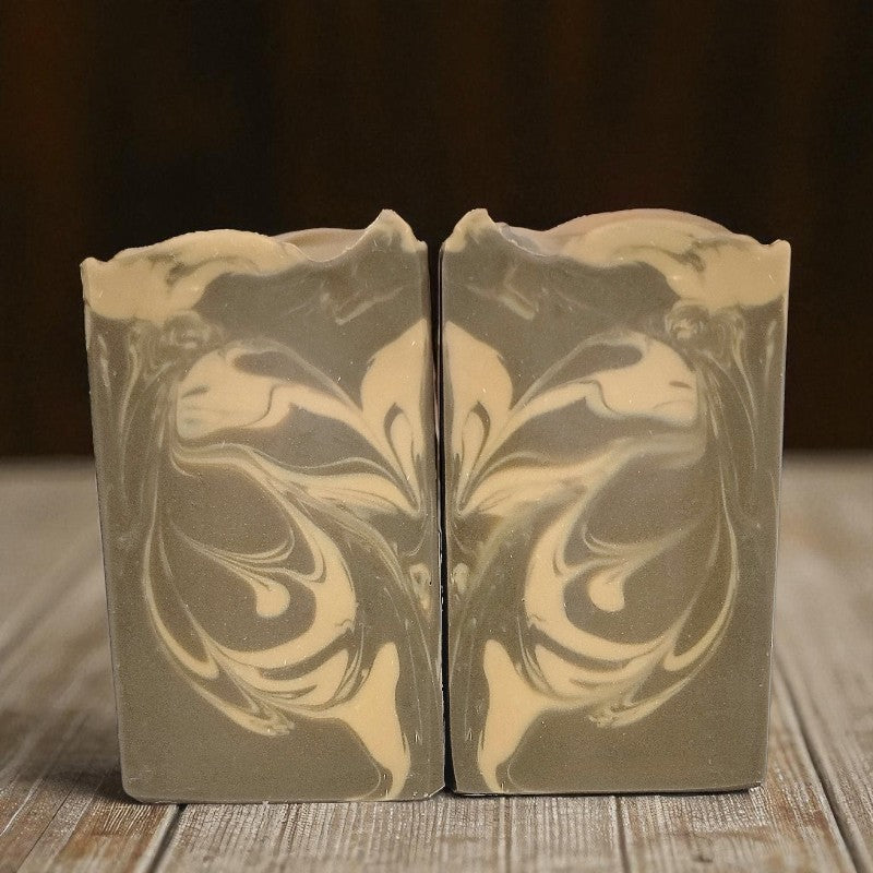 Two brown & cream swirled soap bars on a wooden surface with a dark background