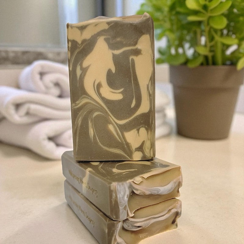 Stack of marbled soap bars on a surface with a plant and towel in the background