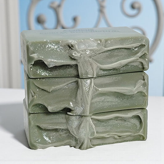 Stack of three green soap bars on a white surface with a decorative metal railing in the background