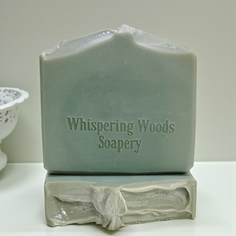 Two bars of soap with 'Whispering Woods Soapery' branding on a white surface