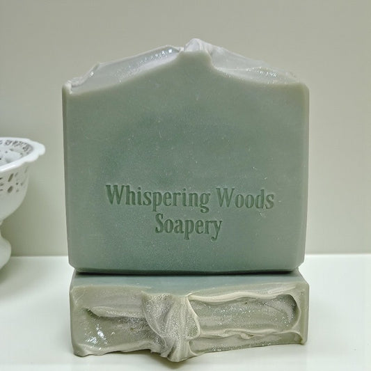 Two bars of soap with 'Whispering Woods Soapery' branding on a white surface
