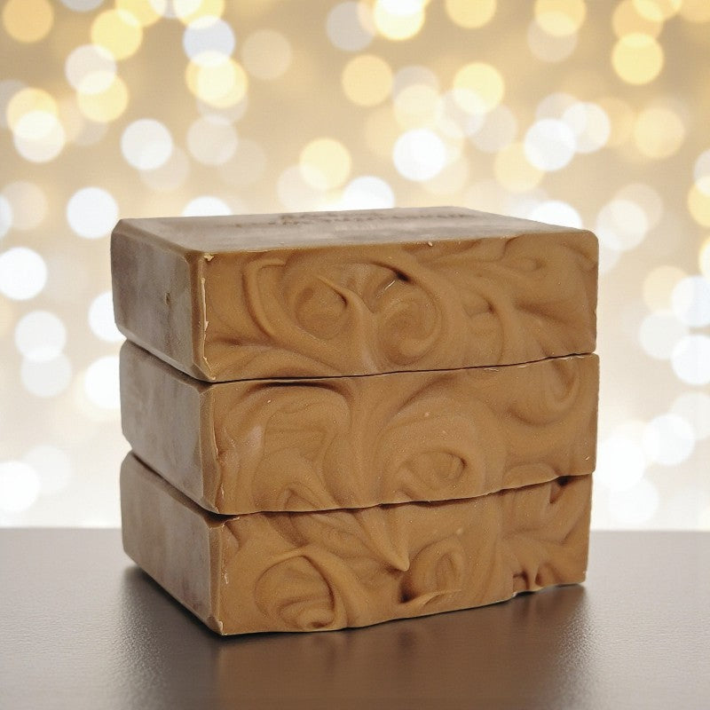 Three bars of brown soap stacked on a reflective surface with a blurred bokeh background