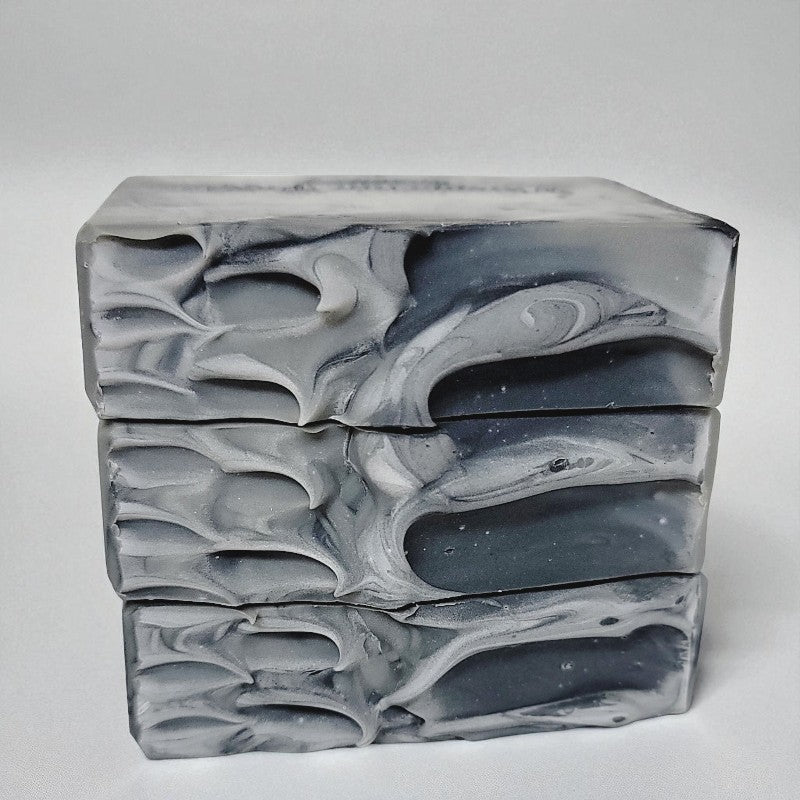 Close-up of gray and black marbled soap tops stacked on a light gray background