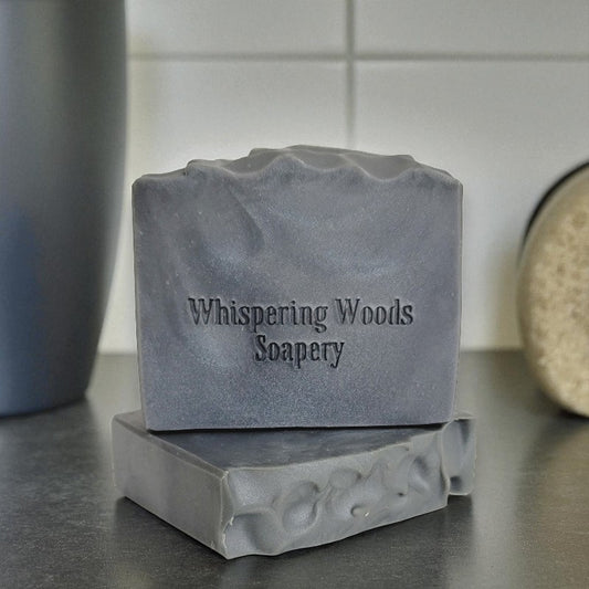 Silvery gray bars of soap with 'Whispering Woods Soapery' branding on a countertop