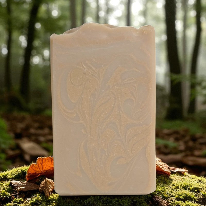 Beautiful tan bar of soap with coppery-gold swirls with a forest in the background